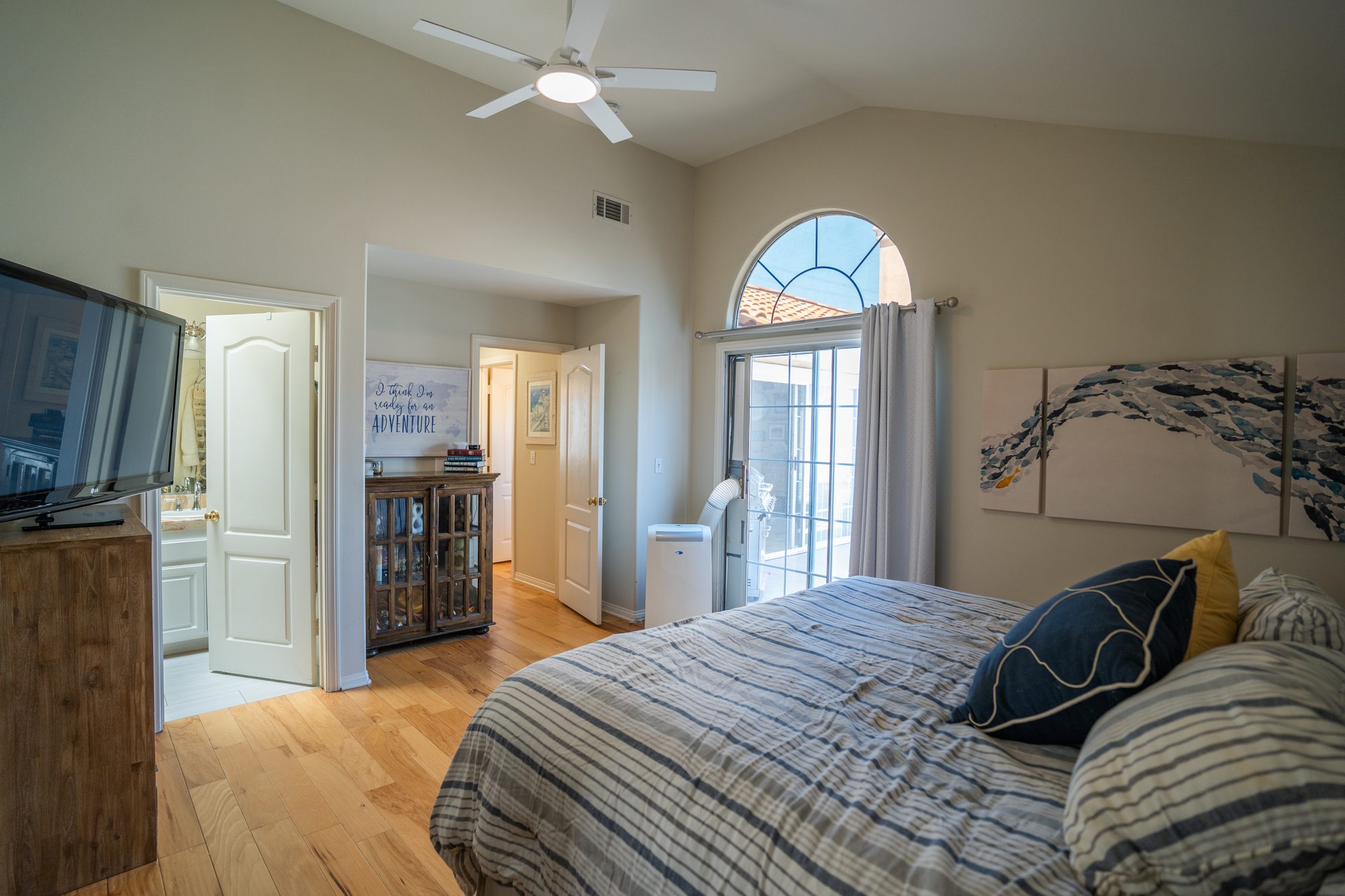 Primary bedroom with vaulted ceiling, arched window, and balcony access
